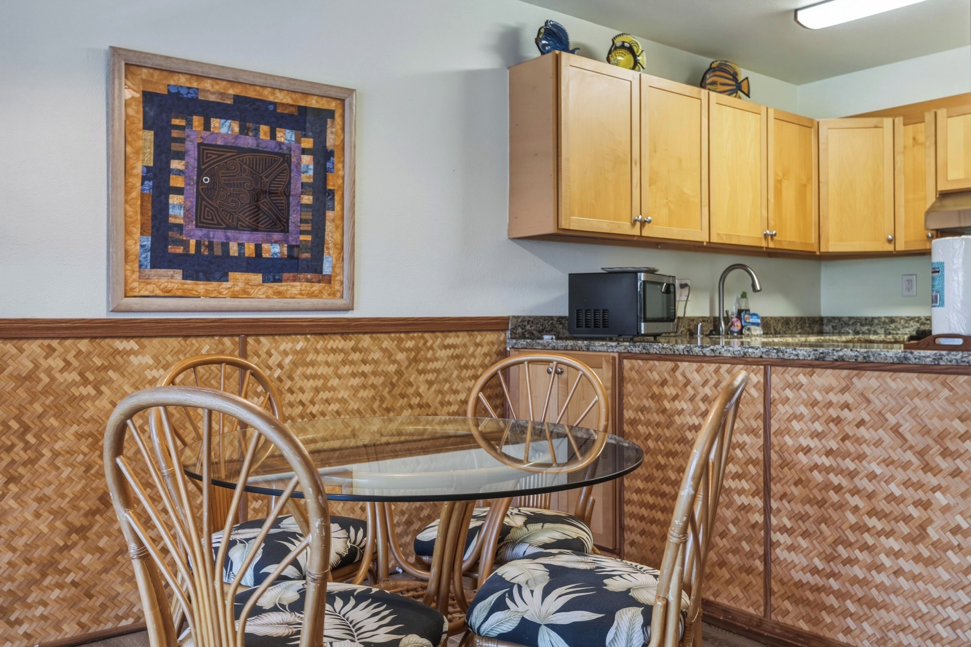 A kitchen with wooden cabinets, a microwave, and a dining area with a glass table and wicker chairs.
