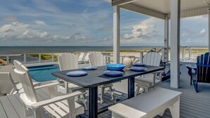 A covered outdoor dining area with a pool view, white chairs, and a table set with blue plates and a pitcher.