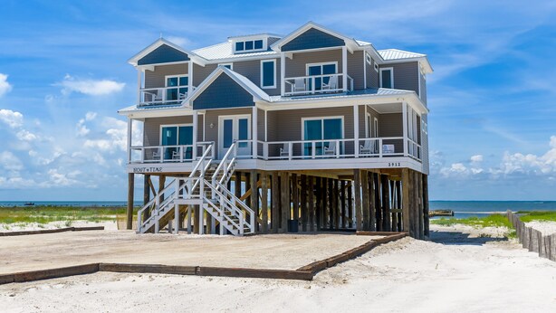 A multi-story beachfront house with a balcony, a staircase, and a view of the ocean.
