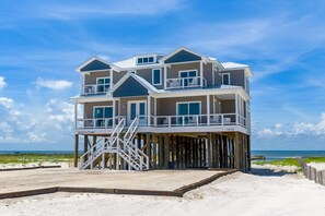 A multi-story beachfront house with a balcony, a staircase, and a view of the ocean.