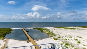 A beach view with a wooden boardwalk leading to the water, a sandy beach, and a clear sky.