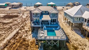 A beachfront property with a large house featuring multiple balconies, a swimming pool, and several beach huts.