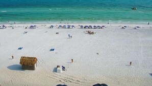 Una spiaggia con sabbia bianca, acque cristalline turchesi e diversi ombrelloni.