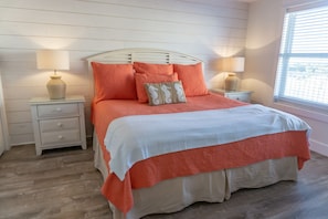 A bedroom with a white headboard, two bedside tables with lamps, a bed with orange bedding, and a window with blinds.