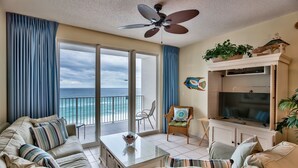 Un ampio soggiorno con balcone vista oceano, una ventola a soffitto e un televisore su un mobile.