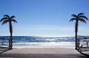 A beach entrance with metal gates and palm trees.