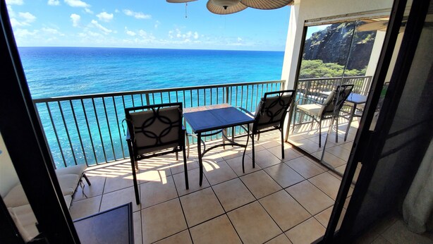 Ein Balkon mit Tisch und Stühlen mit Blick auf das klare, blaue Meer.