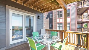 Un espace extérieur abrité, doté d’une table et de chaises en verre, d’une terrasse en bois et offrant une vue sur les bâtiments adjacents.