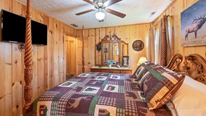 Ein Schlafzimmer mit Holzwandverkleidung, einem Bett, einem Deckenventilator, einem Fernseher und einem Elchgemälde.