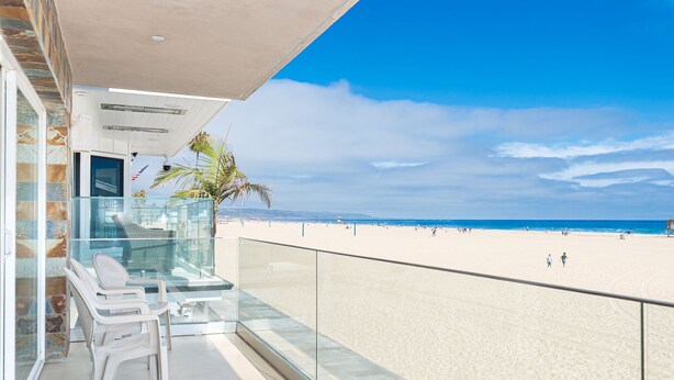 Ein Balkon mit Glasgeländer mit Blick auf einen Strand.