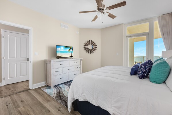A bedroom with a bed, a dresser, a ceiling fan, a wall clock, and a view of the outdoors.