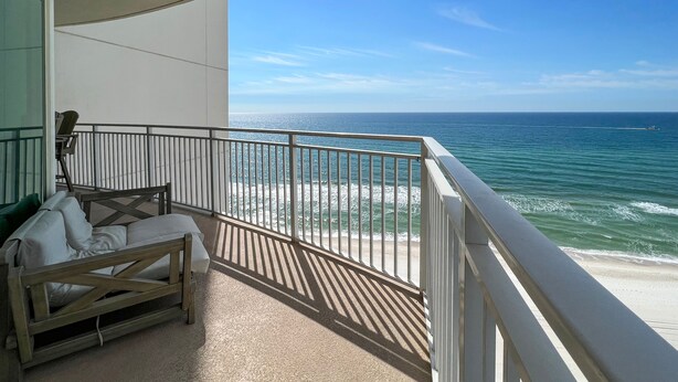 A balcony with a view of the ocean, a wooden bench, and a white railing.