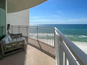 A balcony with a view of the ocean, a wooden bench, and a white railing.