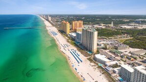 An aerial view of a coastal city with a beach, high-rise buildings, and a pier.