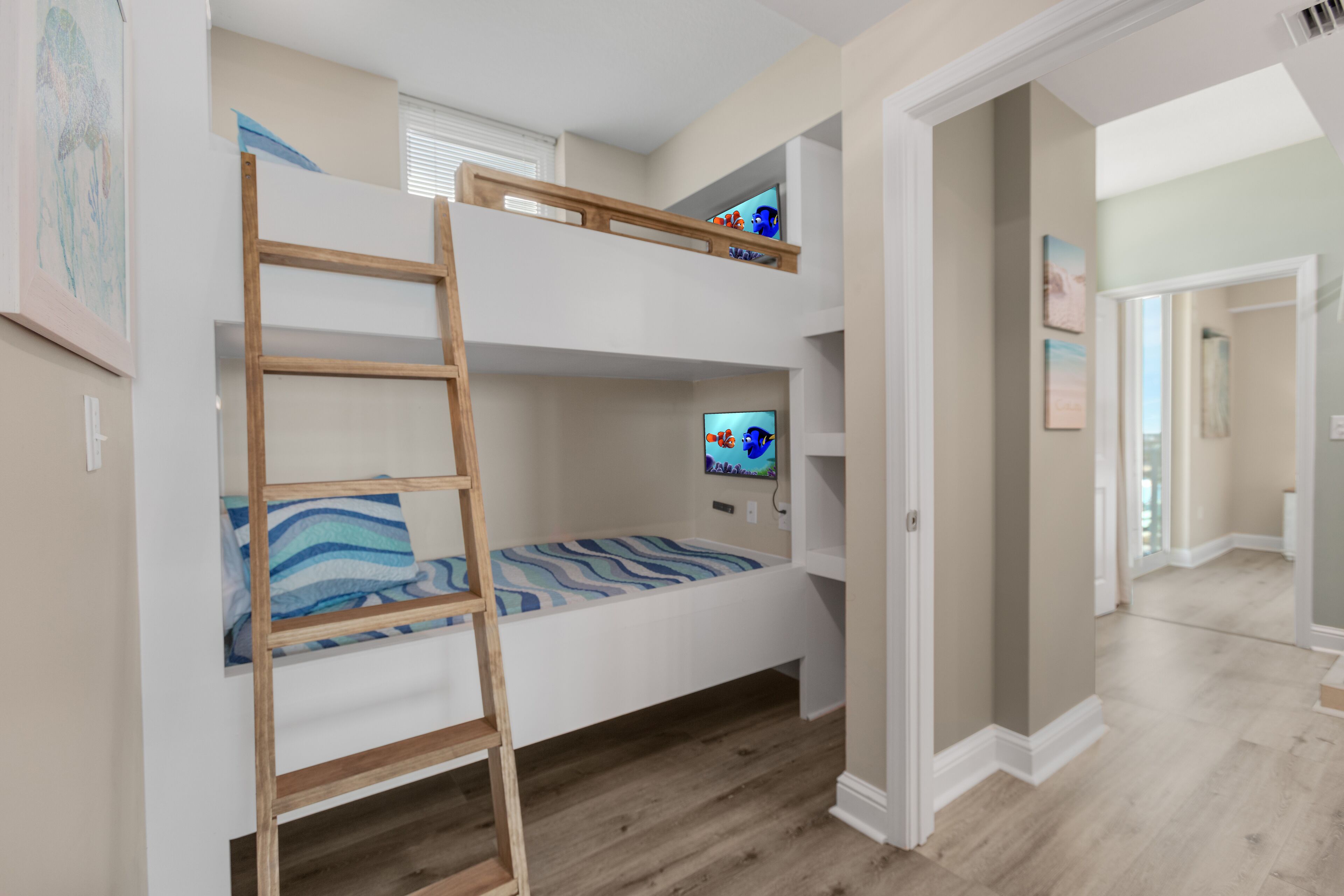 Ein Schlafraum mit Etagenbetten, einer Holzleiter, einem Fernseher im oberen Bett und einem Flur, der in ein weiteres Zimmer führt.