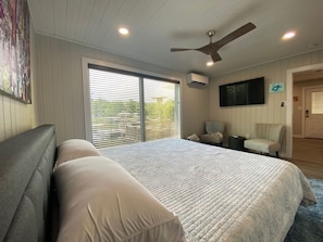 A bedroom with a large bed, a ceiling fan, a TV, and a window with blinds.