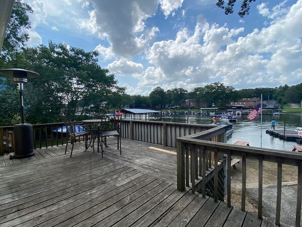 A wooden deck with a railing, a table, chairs, and a lamp.