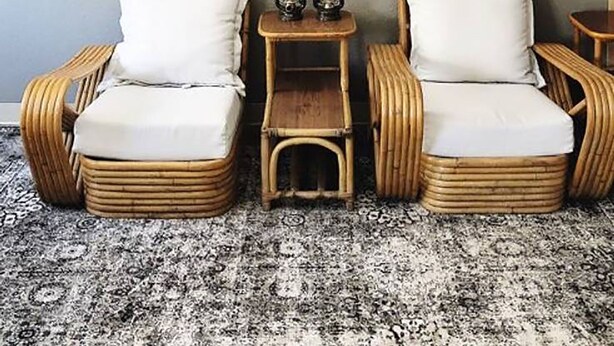 Une pièce comprenant deux fauteuils en osier, une petite table en bois avec des lanternes, et une étagère murale ornée d’objets décoratifs.