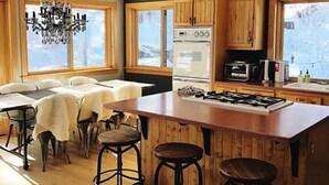 Une cuisine avec des meubles en bois, un grand îlot central doté de tabourets, un lustre et une vue sur l’extérieur grâce à de grandes fenêtres.
