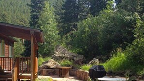 Un espace patio doté d’un sol en pierre, d’une pergola en bois, de mobilier d’extérieur et d’un barbecue.