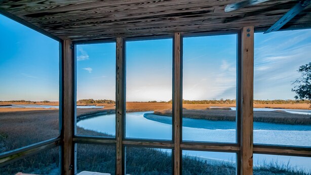 Una habitación con ventanas amplias que dan a un río y una zona pantanosa.