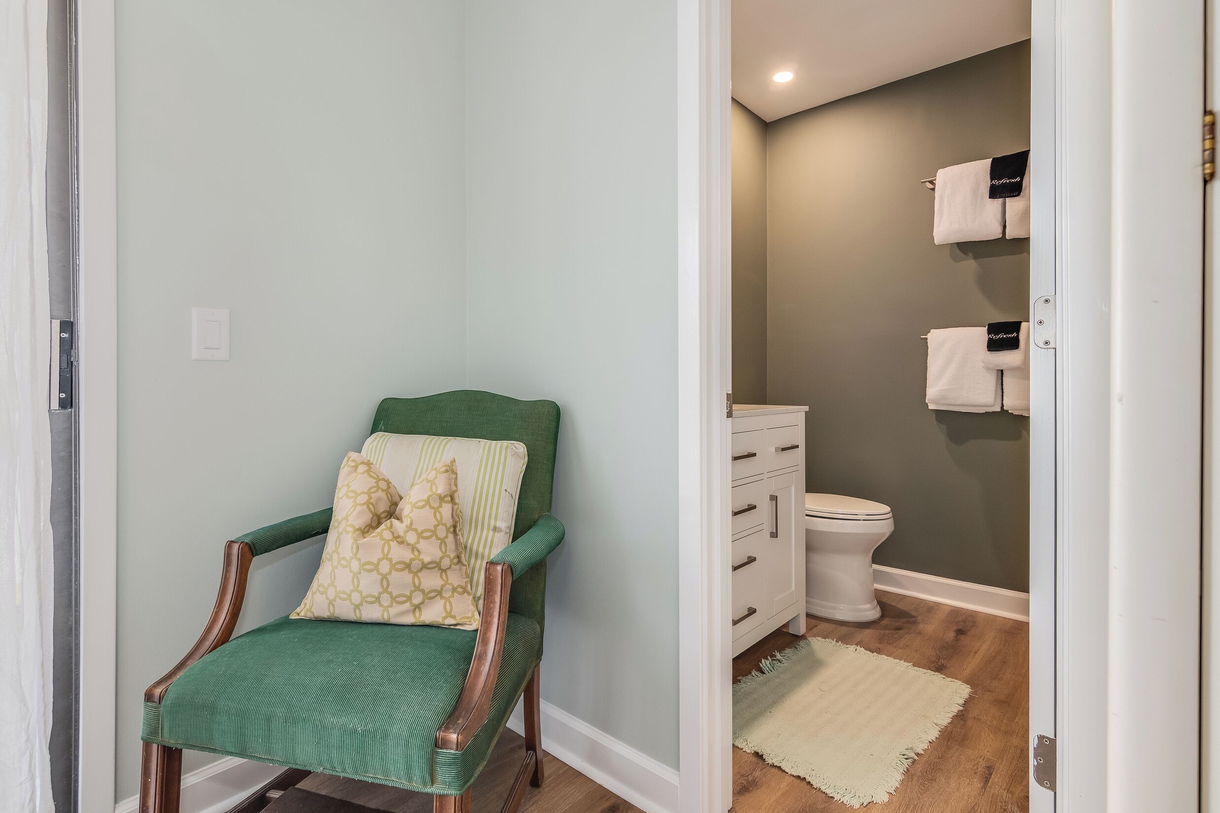 A bathroom with a green chair, a white toilet, and a towel rack.