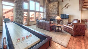 A spacious living room with a shuffleboard table, stone fireplace, leather furniture, and a stone wall.