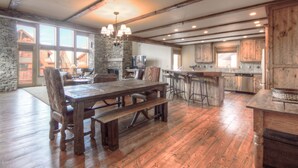 A spacious kitchen with a stone wall, wooden beams, and a large dining table with bar stools.