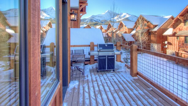 A wooden deck with a grill and outdoor seating, overlooking a snowy mountain landscape.