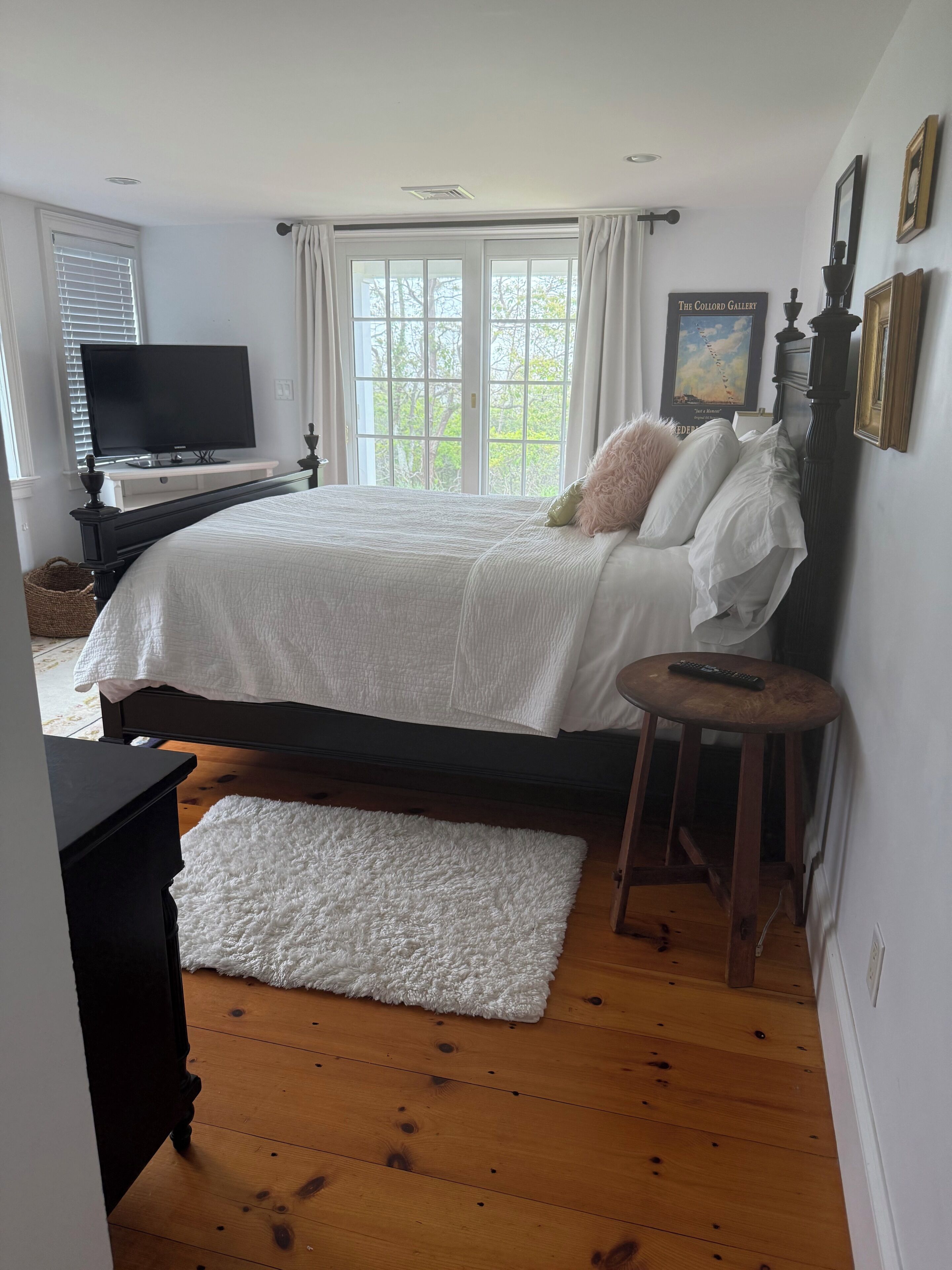 A bedroom with a bed, a television, a window, and a painting on the wall.