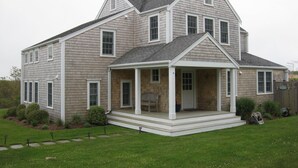A two-story house with a covered porch, a chimney, and a well-maintained lawn. - The Sandbox   Beautiful Home in Tom Nevers (Nantucket)