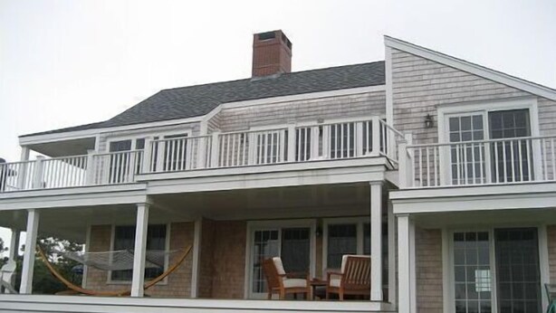 A two-story house with a covered porch, a chimney, and a large window. - The Sandbox   Beautiful Home in Tom Nevers (Nantucket)