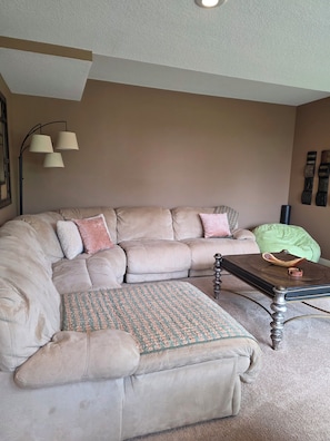 A living room with a sectional sofa, a patterned ottoman, a coffee table, and a floor lamp.
