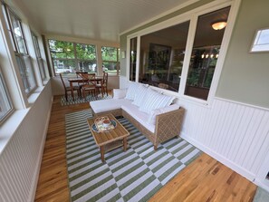 Une véranda aménagée avec un canapé en osier, une table à manger avec des chaises, et une vue sur l’extérieur.