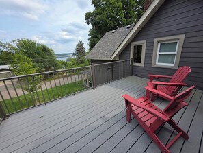 Une terrasse avec une rambarde, une chaise Adirondack rouge et une vue sur un pont et des arbres.
