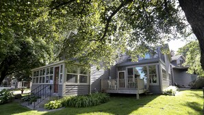 Ein zweistöckiges Haus mit Veranda, kleiner Terrasse und gepflegtem Rasen.