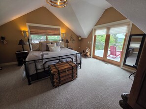 Une chambre avec un grand lit, une commode, une table de chevet, une lampe et une vue sur l’extérieur grâce à une porte-fenêtre coulissante.