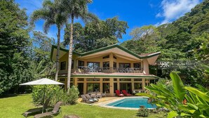 A two-story house with a balcony, a swimming pool, and a well-maintained lawn.