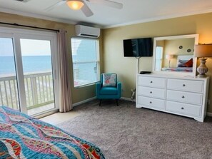 Ein Schlafzimmer mit Bett, Kommode, Stuhl, Fernseher und einem Balkon mit Meerblick.