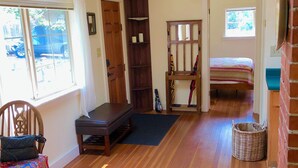 A spacious room with wooden flooring, a bench, a wicker basket, and a bed in the background. - Garden Cottage on College Hill (Eugene)