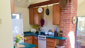 A kitchen with wooden cabinets, a gas stove, a white refrigerator, and a brick wall. - Garden Cottage on College Hill (Eugene)