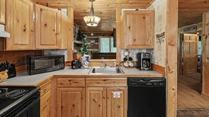 A wooden cabin interior with a kitchen featuring wooden cabinets, a microwave, a toaster, a coffee maker, and a dishwasher. - Matthew11:28~4 mil Pkwy-Dwntwn Pigfrge hot tub, wifi-gas fireplace-NO EXTRA FEES (Pigeon Forge)