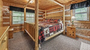 A log cabin bedroom with a four-poster bed, a wooden nightstand, a lamp, and a window with blinds. - Matthew11:28~4 mil Pkwy-Dwntwn Pigfrge hot tub, wifi-gas fireplace-NO EXTRA FEES (Pigeon Forge)