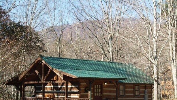 A wooden cabin with a green roof, a porch, and a view of trees and mountains in the background. - Matthew11:28~4 mil Pkwy-Dwntwn Pigfrge hot tub, wifi-gas fireplace-NO EXTRA FEES (Pigeon Forge)