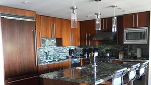 Une cuisine moderne avec des meubles en bois, un grand îlot central doté de tabourets, des appareils en acier inoxydable et un éclairage suspendu.