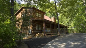 Eine Blockhütte mit Veranda und überdachter Auffahrt, umgeben von Bäumen.
