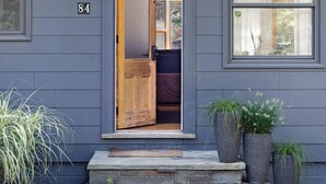 Una casa de exterior gris, una puerta principal de madera y el número 84 en la pared.