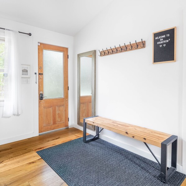 A hallway with a wooden bench, a coat rack, and a welcome sign. - Stunning Custom Designer Home in the Catskills! (Saugerties)
