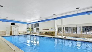 En indendørs swimmingpool med klart, blåt vand, omgivet af en flisebelagt terrasse og en hvid væg med blå detaljer.