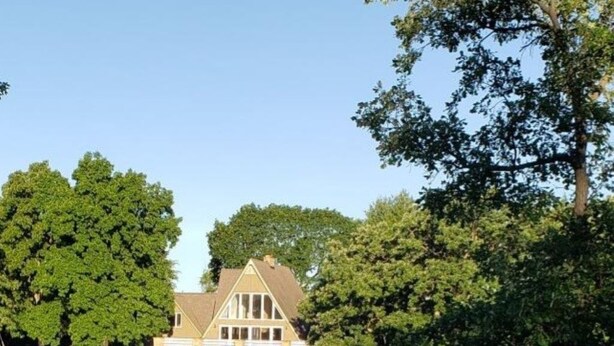 Une maison avec un étang devant, entourée d’arbres.